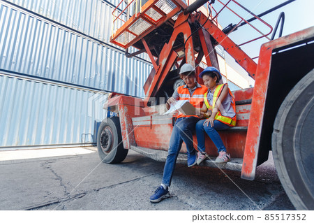 Man engineering and daughters sitting on forklift working with clipboard in container yard. Man engineering and daughters sitting on forklift working with clipboard in container yard. 85517352