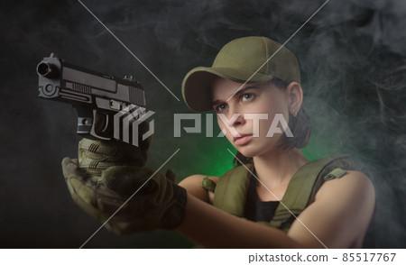 the girl in military special clothes posing with a gun in his hands on a dark background in the haze 85517767