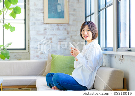 微笑的年輕女子，在客廳裡操作智能手機 85518019