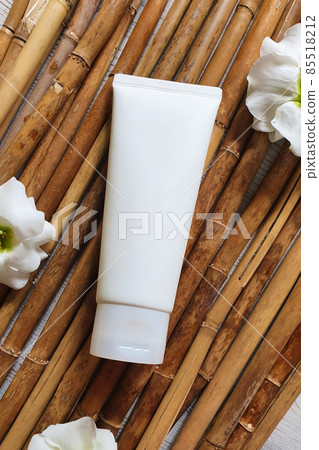 Mockup of white squeeze bottle plastic cosmetic tube for branding of medicine or cosmetics - cream, gel, skin care, toothpaste, moisturizer and white flowers on bamboo or cany background. Mockup of white squeeze bottle plastic cosmetic tube for branding of medicine or cosmetics - cream, gel, skin care, toothpaste, moisturizer and white flowers on bamboo or cany background. 85518212