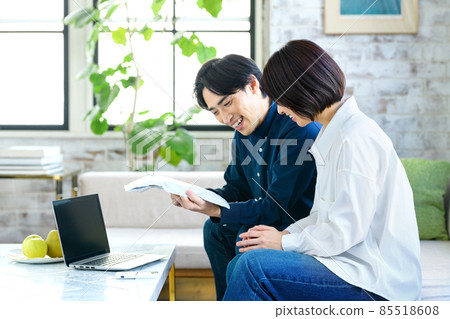 一對年輕夫婦在客廳的電腦前檢查行李 85518608