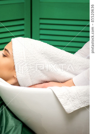 Hairdresser wraps hair of a young caucasian woman in a white towel after washing head in the hairdressing salon. 85520636