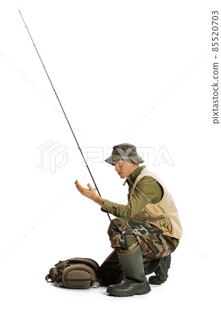 Portrait of young man, professional fisherman with fishing rod, spinning and equipment going to river isolated over white studio background Portrait of young man, professional fisherman with fishing rod, spinning and equipment going to river isolated over white studio background 85520703