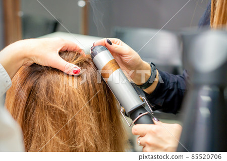 Hands of female hairstylist curls hair client with a curling iron in a hairdressing salon, close up. Hands of female hairstylist curls hair client with a curling iron in a hairdressing salon, close up. 85520706