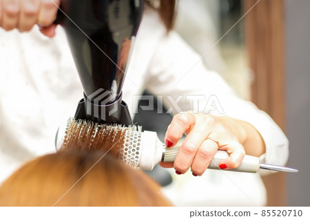 A professional hairdresser is drying long red hair with a hair dryer and round brush, close up. A professional hairdresser is drying long red hair with a hair dryer and round brush, close up. 85520710