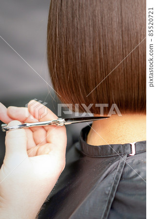 The hairdresser cuts the hair of a brunette woman. Hairstylist is cutting the hair of female client in a professional hair salon, close up. The hairdresser cuts the hair of a brunette woman. Hairstylist is cutting the hair of female client in a professional hair salon, close up. 85520721