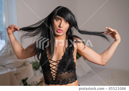 A homosexual guy in black lace underwear and a wig grimaces at the camera. A homosexual guy in black lace underwear and a wig grimaces at the camera. 85521086