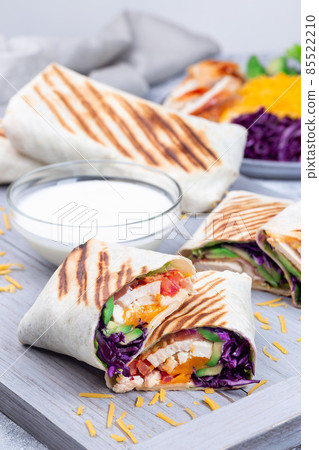 Chicken wraps with red cabbage, avocado, tomato, lettuce, cheddar cheese, on a wooden tray 85522210