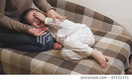 Little child plays with mommy and laughs while lying on the couch. Happy girl rejoices at mom. A daughter and a woman are playing in the children's room. Mothers Day. Parents' love for kid. Upbringing 85522331