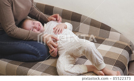 Little child plays with mommy and laughs while lying on the couch. Happy girl rejoices at mom. A daughter and a woman are playing in the children's room. Mothers Day. Parents' love for kid. Upbringing Little child plays with mommy and laughs while lying on the couch. Happy girl rejoices at mom. A daughter and a woman are playing in the children's room. Mothers Day. Parents' love for kid. Upbringing 85522373