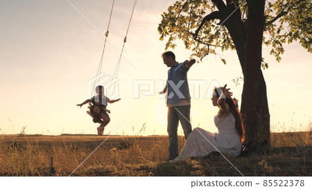 Happy little child with teddy rides on a swing with his parents at sunset in the park. Mom, daughter and dad are having fun at dawn. Happy family life concept. Kid with his beloved mother and father Happy little child with teddy rides on a swing with his parents at sunset in the park. Mom, daughter and dad are having fun at dawn. Happy family life concept. Kid with his beloved mother and father 85522378