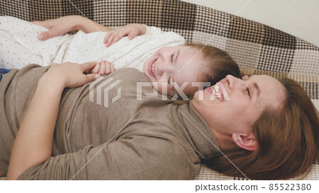 Little child plays with mommy and laughs while lying on the couch. Happy girl rejoices at mom. A daughter and a woman are playing in the children's room. Mothers Day. Parents' love for kid. Upbringing Little child plays with mommy and laughs while lying on the couch. Happy girl rejoices at mom. A daughter and a woman are playing in the children's room. Mothers Day. Parents' love for kid. Upbringing 85522380