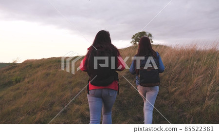 Girls with backpacks climb high up the mountain helping each other on a hiking trip. Women spend the weekend traveling in nature overcoming obstacles. Teamwork. Friends are looking for adventure Girls with backpacks climb high up the mountain helping each other on a hiking trip. Women spend the weekend traveling in nature overcoming obstacles. Teamwork. Friends are looking for adventure 85522381