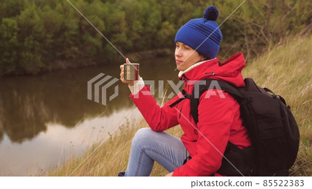 The girl drinks tea from a mug sitting on a high mountain and enjoying nature in the park. Woman traveler looking for adventure. Relax on the hike. Long distance hiking trips. Human explorer of 85522383