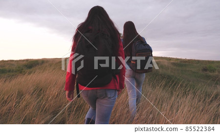 Girls with backpacks climb high up the mountain helping each other on a hiking trip. Women spend the weekend traveling in nature overcoming obstacles. Teamwork. Friends are looking for adventure 85522384
