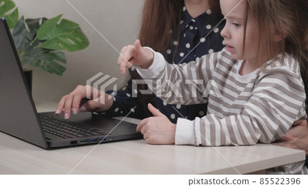 Business woman freelancer working at a laptop at home with a small child in her arms, typing text on a computer keyboard and looking at the monitor display, kid sits on her mother s lap and smiles 85522396