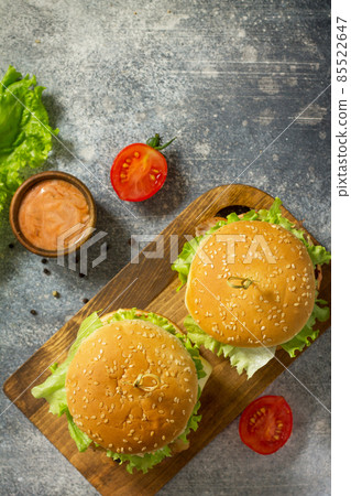 Delicious grilled burgers, hamburger sandwich with cutlet of chicken meat, melted cheese, tomatoes and bacon on a wooden board. Top view flat lay. Free space for your text. Delicious grilled burgers, hamburger sandwich with cutlet of chicken meat, melted cheese, tomatoes and bacon on a wooden board. Top view flat lay. Free space for your text. 85522647