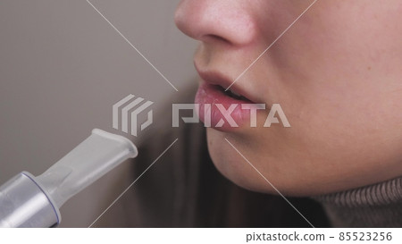 The girl breathes in a solution for inhalation of lungs. A young woman in quarantine treats a cough by inhaling steam with medicine. Treatment of a person at home with professional equipment for colds 85523256