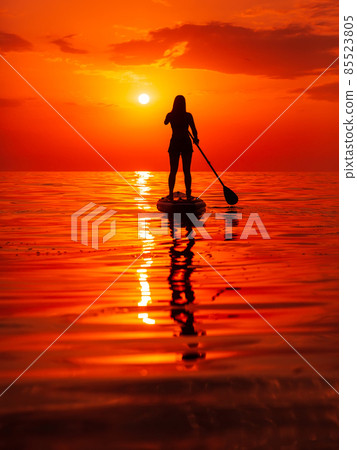 Silhouette of woman on stand up paddle board at quiet sea. Woman posing on SUP board and bright sunset with reflection Silhouette of woman on stand up paddle board at quiet sea. Woman posing on SUP board and bright sunset with reflection 85523805