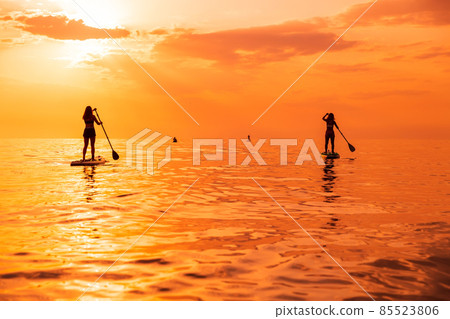 Travelers on stand up paddle board at quiet sea with sunset or sunrise. Girls on Red Paddle sup board and sunset Travelers on stand up paddle board at quiet sea with sunset or sunrise. Girls on Red Paddle sup board and sunset 85523806