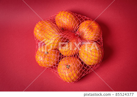 Mesh with tangerines on a red festive background. Mesh with tangerines on a red festive background. 85524377