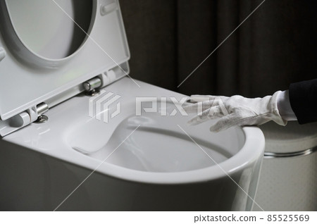 Housekeeper in a neat white apron standing scrubbing out a toilet with a brush. 85525569