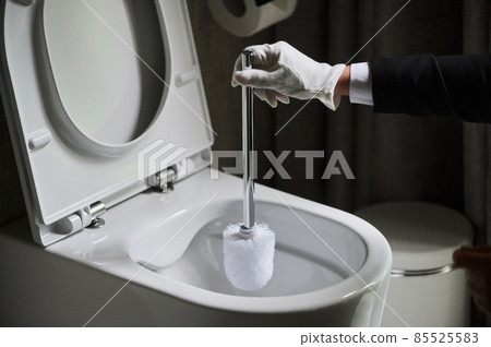 Housekeeper in a neat white apron standing scrubbing out a toilet with a brush. Housekeeper in a neat white apron standing scrubbing out a toilet with a brush. 85525583