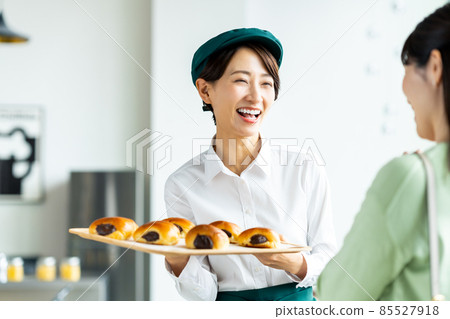 A middle-aged female clerk recommending freshly baked bread to a customer 85527918