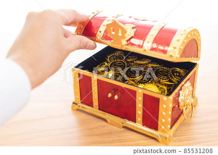 A man's hand that opens a treasure box containing a lot of gold coins. 85531208