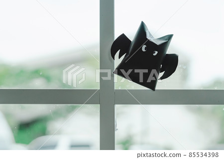 Origami bat made of black paper, isolated on glass window or door background. Dark paper ghost Halloween party concept origami paper bat. The figure of black paper bat flying over white background. Origami bat made of black paper, isolated on glass window or door background. Dark paper ghost Halloween party concept origami paper bat. The figure of black paper bat flying over white background. 85534398