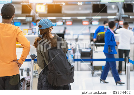 Back view of airline passenger wear face mask to prevent Corona virus (Covid-19) wait to check in counter in airport with staff wear face mask. New normal concept of travel after Covid-19 pandemic. 85534462