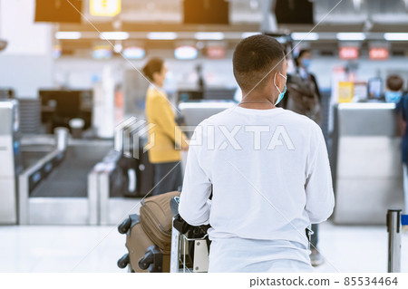 Back view of airline passenger wear face mask to prevent Corona virus (Covid-19) wait to check in counter in airport with staff wear face mask. New normal concept of travel after Covid-19 pandemic. 85534464