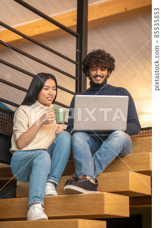 Man and woman looking at laptop sitting on stairs Man and woman looking at laptop sitting on stairs 85535853
