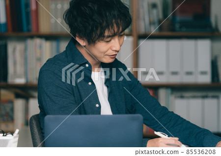 A man writing in front of a computer 85536208