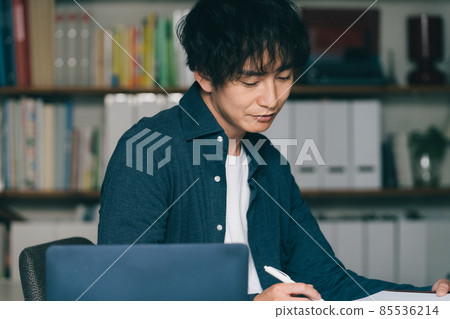 A man writing in front of a computer 85536214