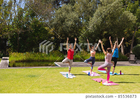 Female instructor teaching yoga to men and woman in public park on sunny day Female instructor teaching yoga to men and woman in public park on sunny day 85536873