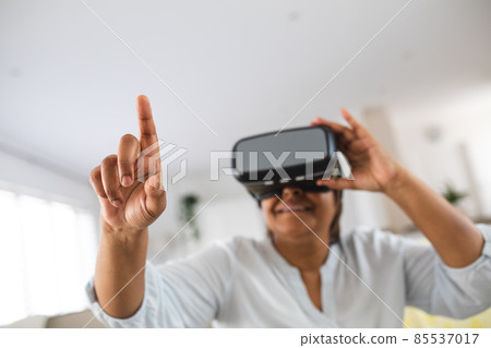 African american senior woman pointing while wearing virtual reality simulator at home, copy space African american senior woman pointing while wearing virtual reality simulator at home, copy space 85537017