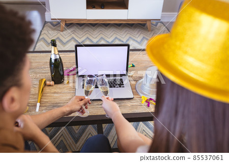 Biracial couple toasting champagne flutes on video call through laptop with blank screen Biracial couple toasting champagne flutes on video call through laptop with blank screen 85537061
