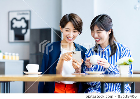 Middle-aged woman looking at a smartphone with a friend at a cafe Middle-aged woman looking at a smartphone with a friend at a cafe 85539400