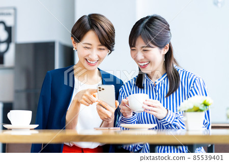 Middle-aged woman looking at a smartphone with a friend at a cafe 85539401