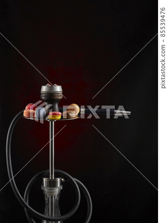 Modern hookah decorated with macaroon of various colors on a dark background. Vertical inage. The culture of serving shisha. Modern hookah decorated with macaroon of various colors on a dark background. Vertical inage. The culture of serving shisha. 85539476