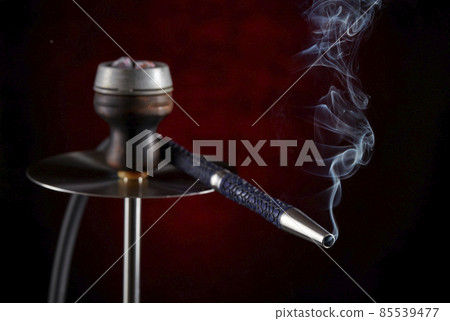 Smoke streaming from the mouthpiece of a modern hookah, on a beautiful dark background. Smoking shisha. 85539477