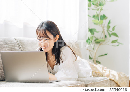 A woman using a computer while lying on the sofa 85540618