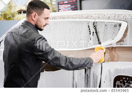Back view of young man washing car on carwash station outdoor. Handsome worker cleaning automobile, using sponge and soap. Back view of young man washing car on carwash station outdoor. Handsome worker cleaning automobile, using sponge and soap. 85543965
