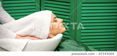 Hairdresser wraps hair of a young caucasian woman in a white towel after washing head in the hairdressing salon. Hairdresser wraps hair of a young caucasian woman in a white towel after washing head in the hairdressing salon. 85545004