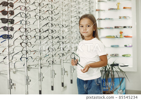 Little girl choosing glasses at optics store 85545234