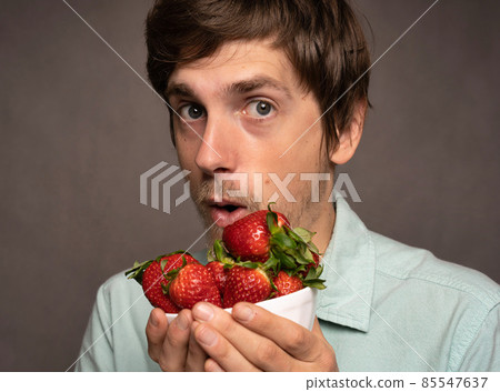Young man with strawberries on grey Young man with strawberries on grey 85547637