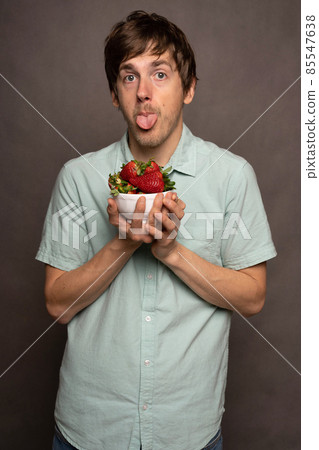 Young man with strawberries on grey Young man with strawberries on grey 85547638