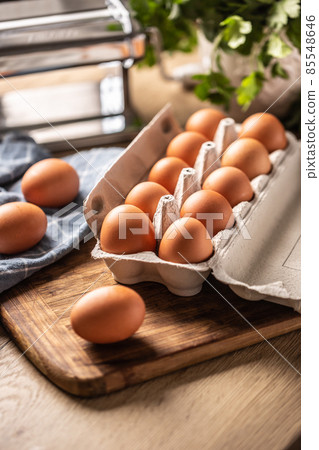 Eggs in a cardboard box on a wooden board in the kitchen. 85548646