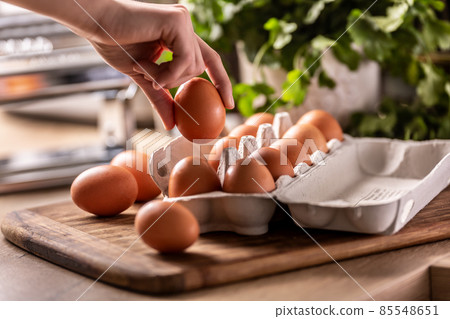 Female hand picks an egg with a carton box lying on the kitchen counter. Female hand picks an egg with a carton box lying on the kitchen counter. 85548651